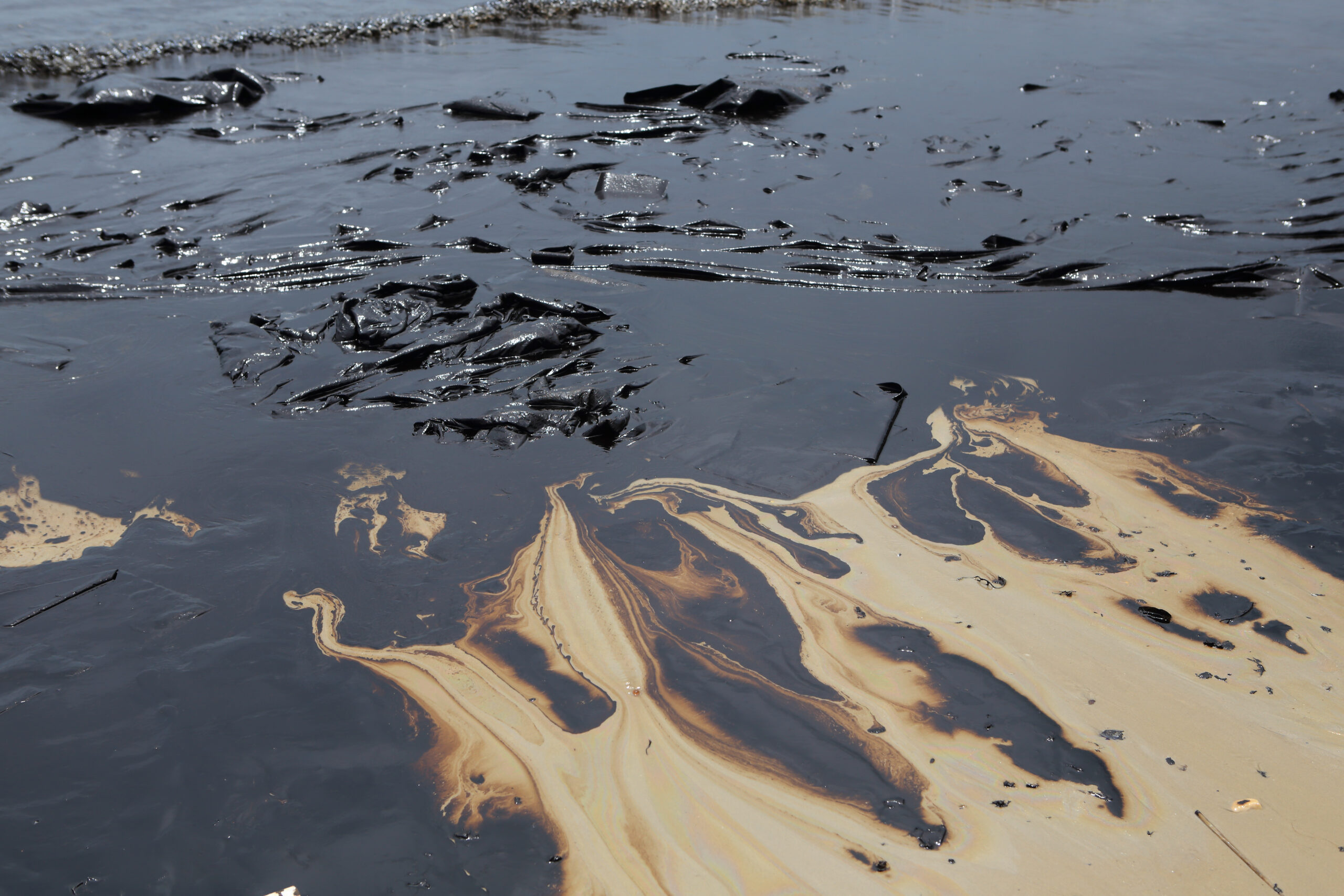 Derrame de petróleo en la costa, con manchas negras y aceitosas sobre la arena y el agua, símbolo de contaminación marina.