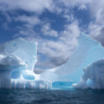 Gran iceberg flotando en aguas del océano Austral bajo un cielo parcialmente nublado, símbolo del deshielo antártico y su impacto climático global.