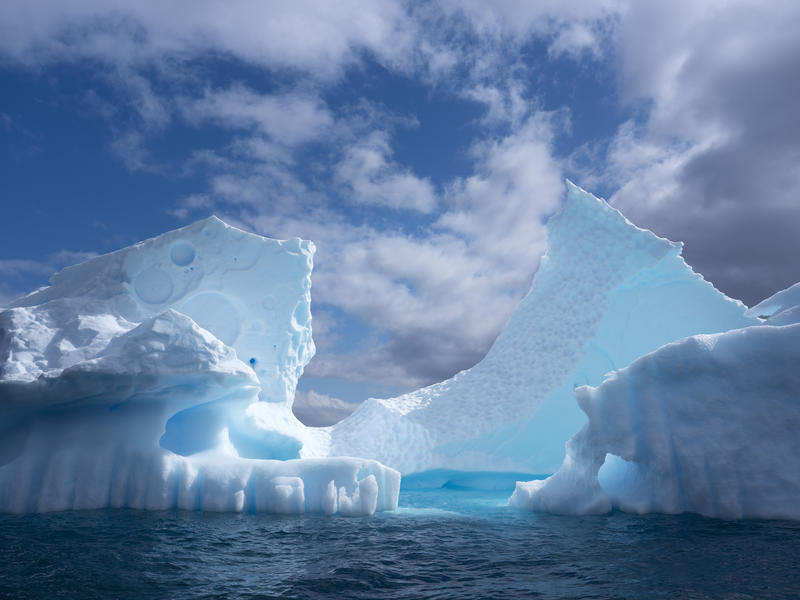 Gran iceberg flotando en aguas del océano Austral bajo un cielo parcialmente nublado, símbolo del deshielo antártico y su impacto climático global.