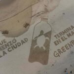 Intervención artística en una playa con forma de botella plástica y una tortuga en su interior; el mensaje en la arena dice: "Lo que comenzó en la ciudad termina en el mar – Greenpeace".