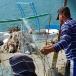 Pescadores manipulando redes en un muelle frente al mar, en el marco de un proyecto colaborativo para la conservación marina en el Mediterráneo.