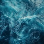 Vista aérea del océano con oleaje turbulento y remolinos de espuma blanca, simbolizando el dinamismo y la fuerza de la transformación geológica.