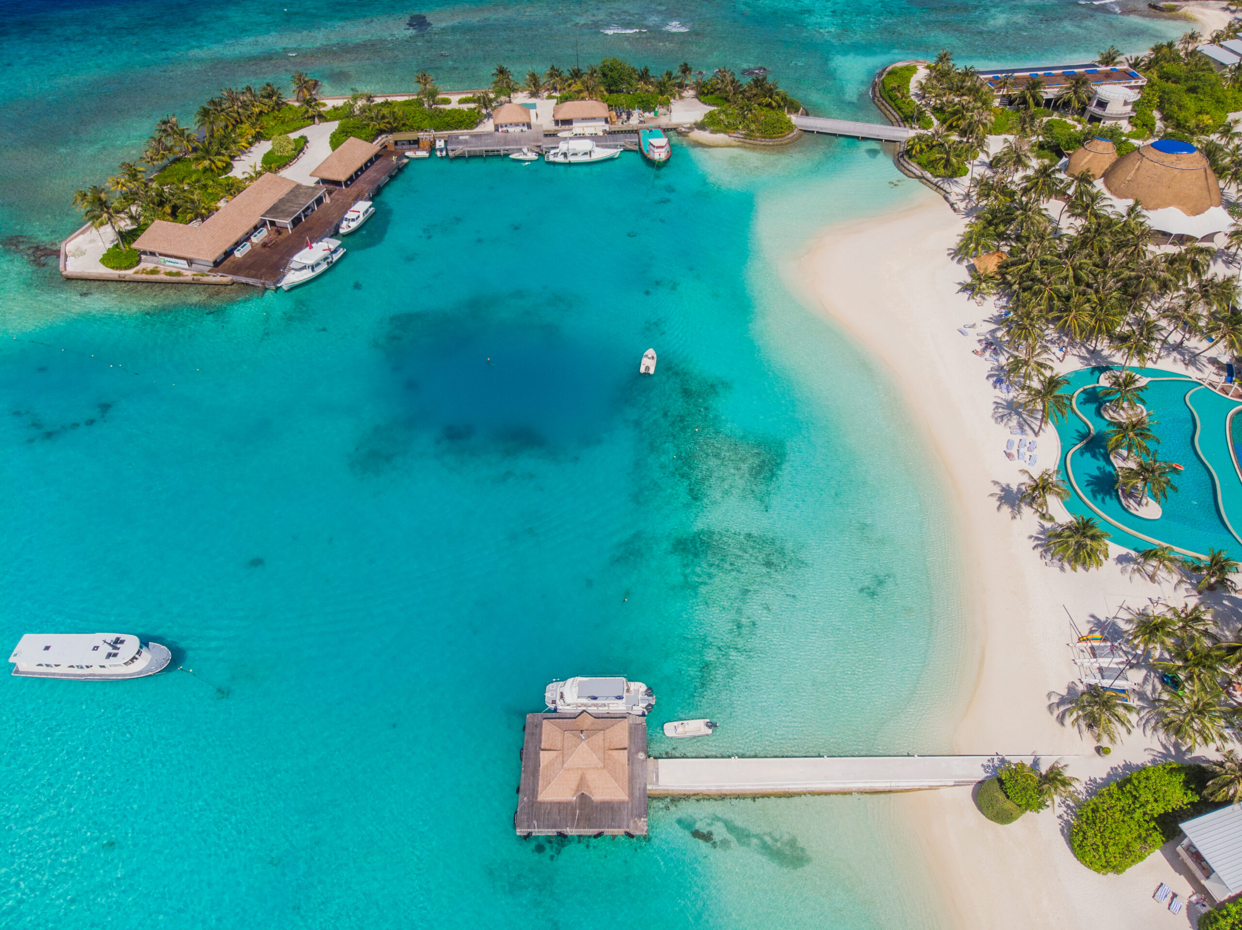 Vista aérea de una playa paradisíaca con hoteles de lujo y aguas cristalinas, rodeada de arrecifes de coral y embarcaciones turísticas.
